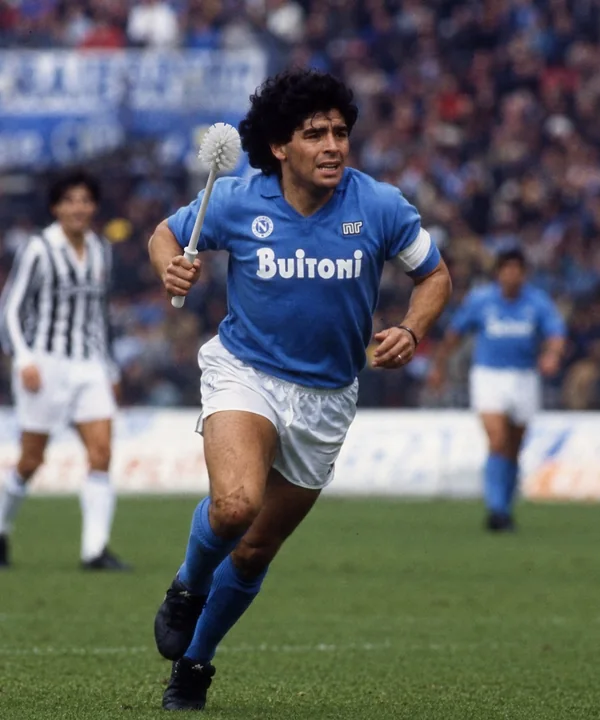 Parodic archive portrait of Diego Maradona carrying a Toilet Brush across the football pitch